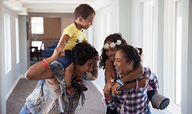 Ronald McDonald House family, Vasco Gonzalez and mom Antuane playing, a boy carried sitting on one woman's shoulder and a girl carried on the back of another